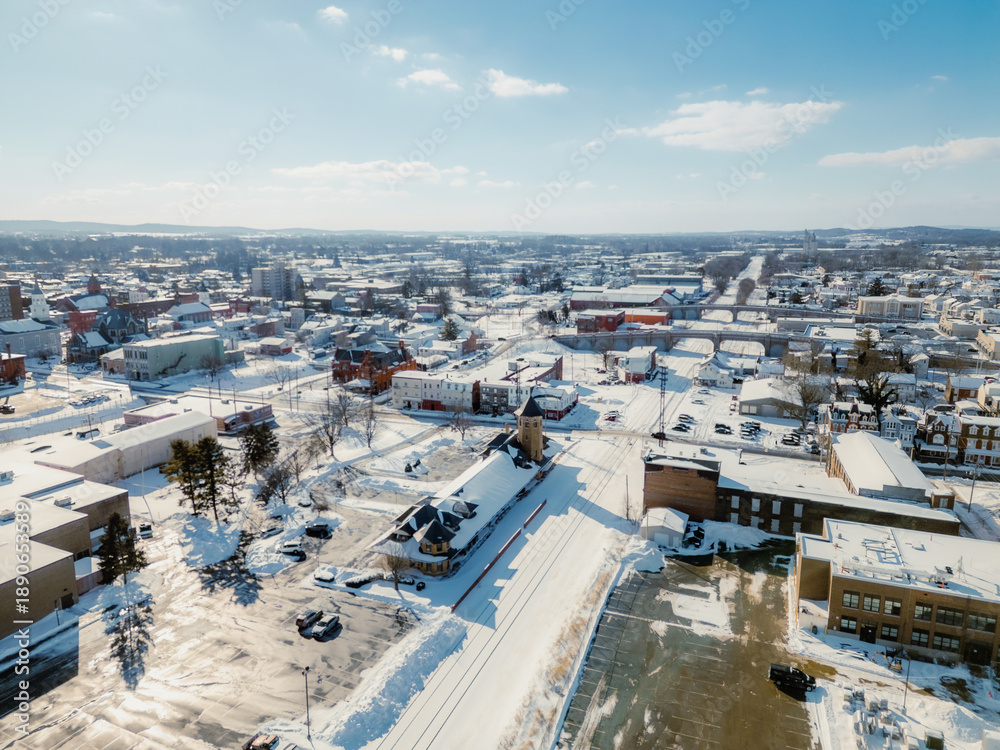 Fototapeta premium High angle aerial view of a city covered in deep white snow under a bright clear blue sky.