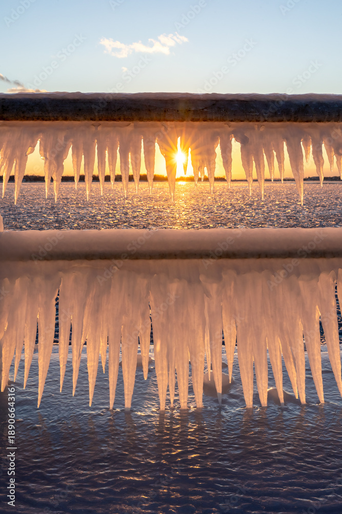 Fototapeta premium Icicles forming on a rail at a frozen pier at sunset - Polson Pier, Toronto Ontario
