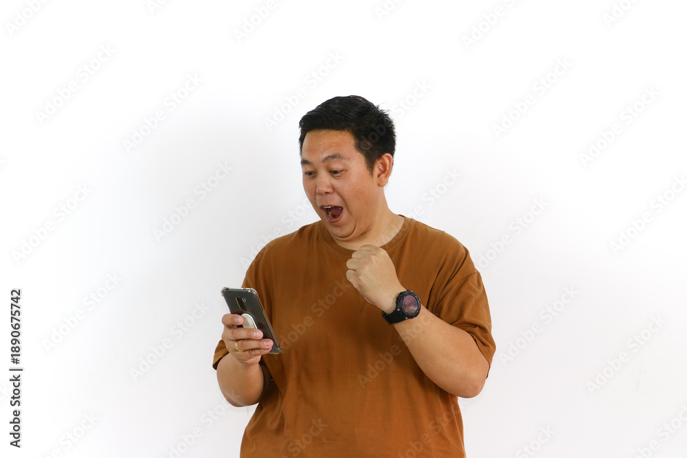 Fototapeta premium An Asian male individual reacting with a winning gesture and excited facial expression while using a smartphone.
