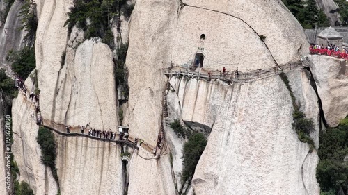 Aerial video close-up of the Longkong plank path at Mount Hua, narrow wooden walkway clinging to sheer cliffs, with hikers navigating the dramatic mountain route. China