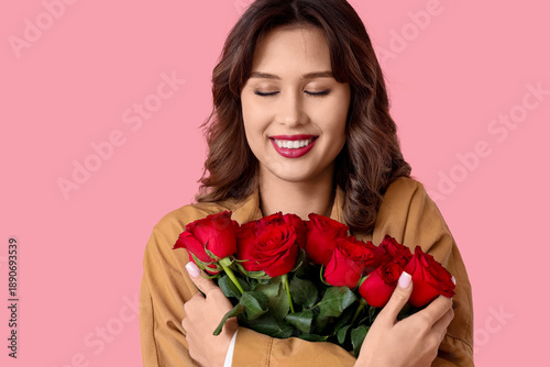 Happy young woman with bouquet of red rose flowers on pink background