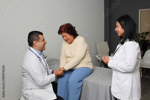 80-year-old Latina woman consults with a geriatrician doctor and her assistant in the office, laugh and enjoy the check-up