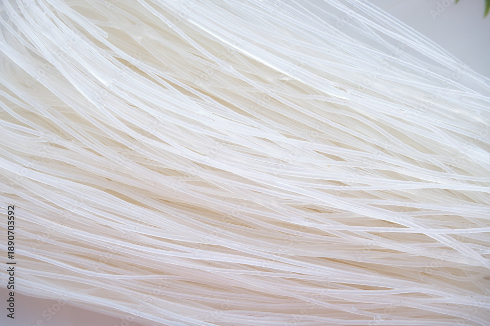 Obraz premium A textured macro shot of dry funchose or rice vermicelli. The thin, translucent white strands are tightly interwoven, creating an abstract linear pattern.