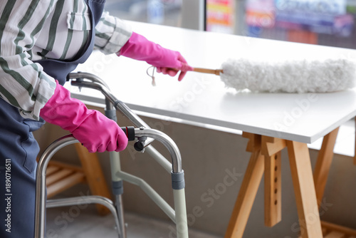 Foto Woman with walker and pp-duster cleaning table at home