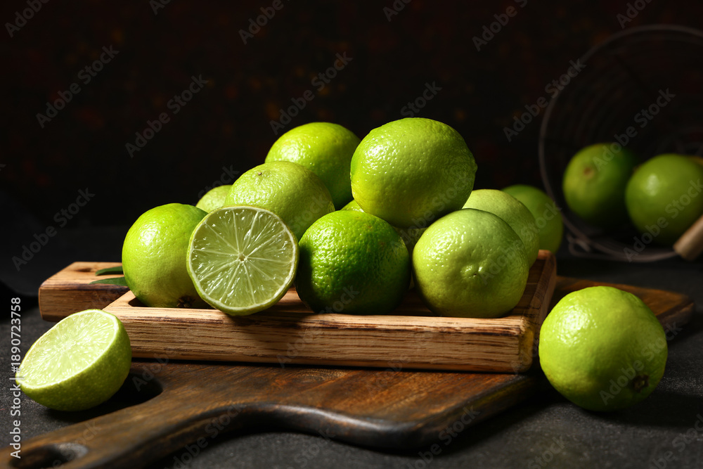 Fototapeta premium Wooden board with fresh ripe limes on black background