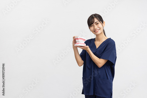 Smiling Young Woman in Navy Medical Scrubs Holding Dental Model on White Background
