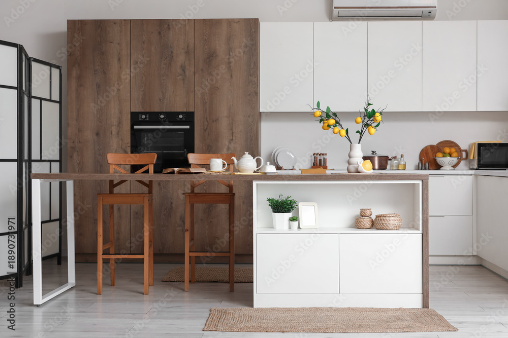 Fototapeta premium Interior of kitchen with counter, chairs, oven, teapot and artificial lemons branches in vase on table