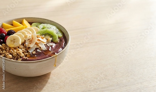 A vibrant acai bowl topped with fresh fruits, granola, and coconut flakes sits on a light wooden table, perfect for a healthy breakfast or snack.