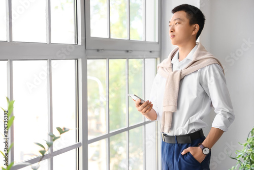 Chinese businessman with mobile phone near window in office Free Download Chinese businessman with mobile phone near window in office - GFXLoad