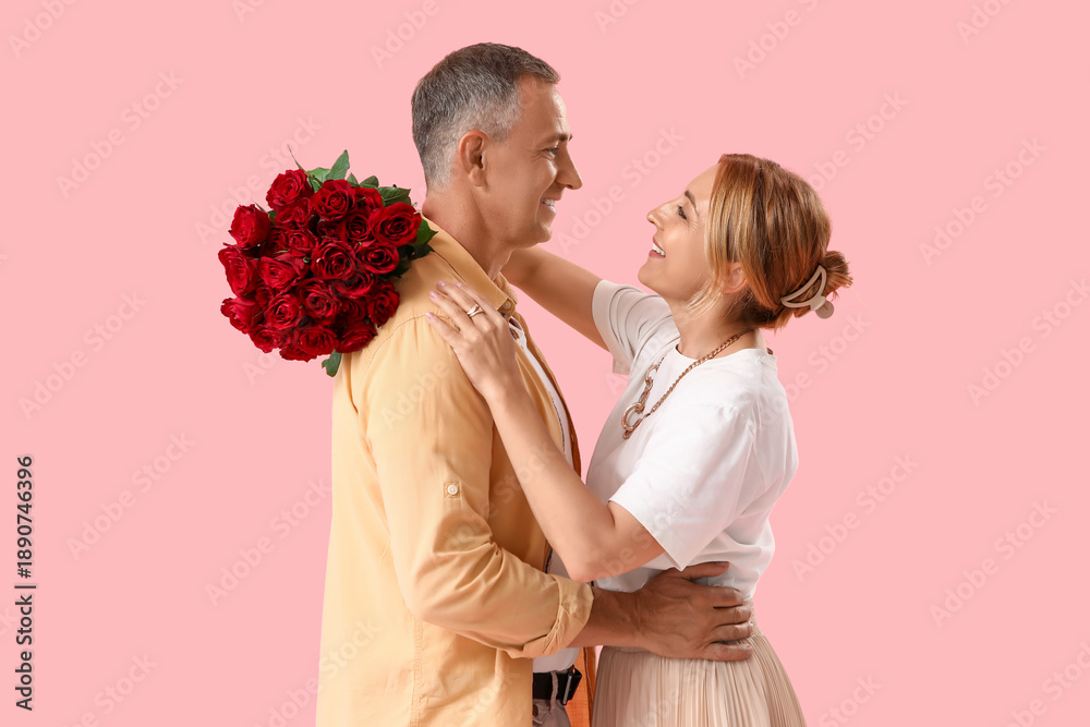 © Pixel-Shot - Happy mature couple with bouquet of roses hugging on pink background. Valentine's Day celebration