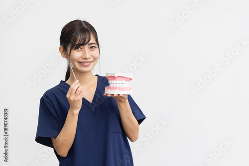 Smiling Young Woman in Navy Medical Scrubs Holding Dental Model and Dental Tool on White Background