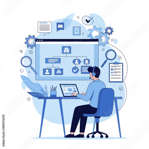 A man sitting at a desk working on a laptop with a large computer screen behind him displaying various icons on a blue background