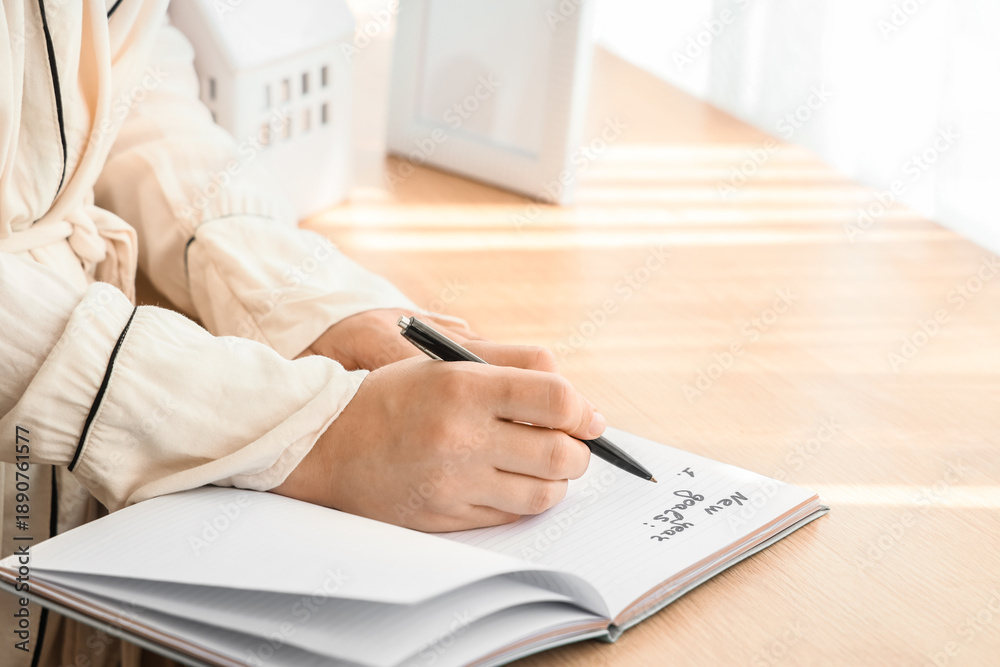 Fototapeta premium Young woman writing New Year goals at home, closeup