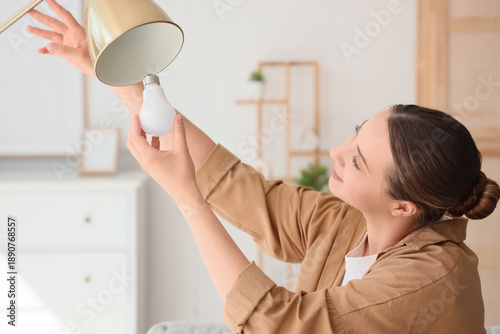 Fotografi Young woman screwing light bulb into standard lamp at home