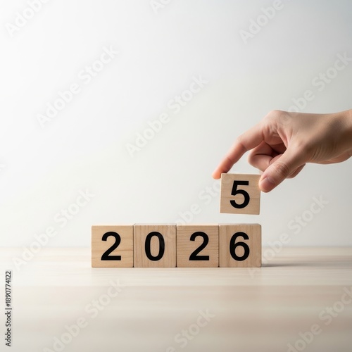 Hand placing wooden block with number 5 above 2026 blocks