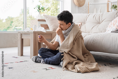 Ill teenage boy with thermometer coughing at home