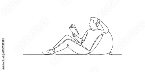 A young man relaxes comfortably on a bean bag chair while engrossed in reading a book