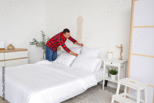 Young man making bed in bed...