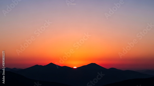 Breathtaking mountain sunset with the golden sun dipping below rugged peaks, painting the sky with vibrant fiery orange, warm amber, and deep twilight purple hues