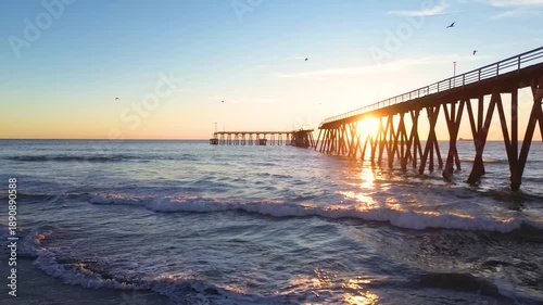 Calm waves rolling onto the shore with a long wooden pier during a beautiful sunset in rosarito