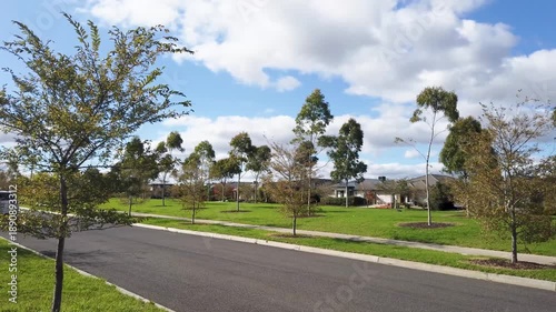 Wide suburban street lined with young trees and open green spaces in a newly developed residential estate, with modern houses nearby. Wyndham Vale, Melbourne, Australia.