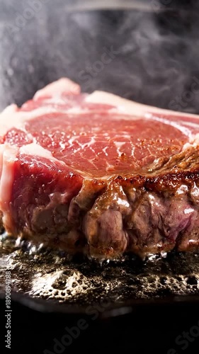 Dramatic close-up of a thick raw ribeye steak sizzling vigorously in hot bubbling fat, producing rising smoke and steam during intense searing on a bl