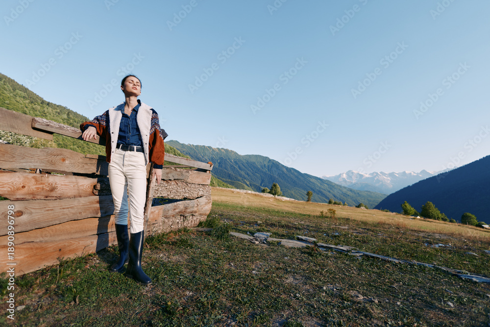 Fototapeta premium Woman hiking in nature near a wooden fence on a mountain meadow, standing with backpack and boots while enjoying a scenic view and fresh air during a peaceful outdoor adventure.