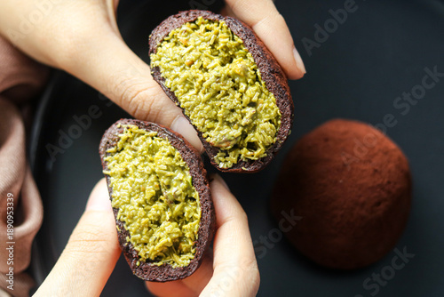 Foto Hand holding a Dubai Chewy Cookie with the chewy outer layer opened to reveal the filling of pistachio and kataifi