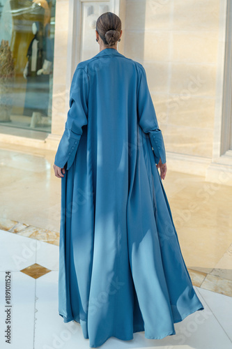 Qatar, Doha, 17.10.2022: Rear view of a woman in a long blue abaya standing in an elegant architectural interior.
