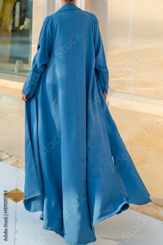 Qatar, Doha, 17.10.2022: Rear view of a woman in a long blue abaya standing in an elegant architectural interior.