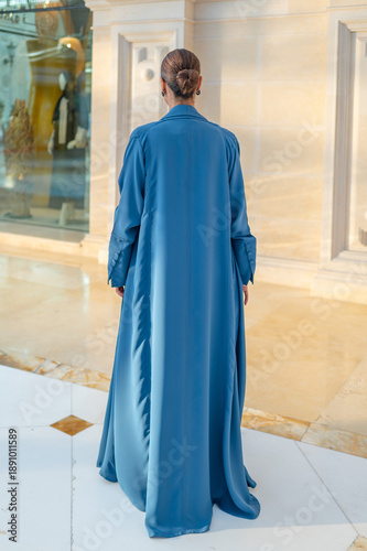 Qatar, Doha, 17.10.2022: Rear view of a woman in a long blue abaya standing in an elegant architectural interior.