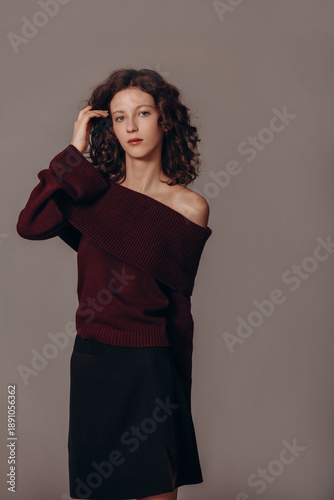 Fotografie The model is a young beautiful brunette girl with curls on a gray background in