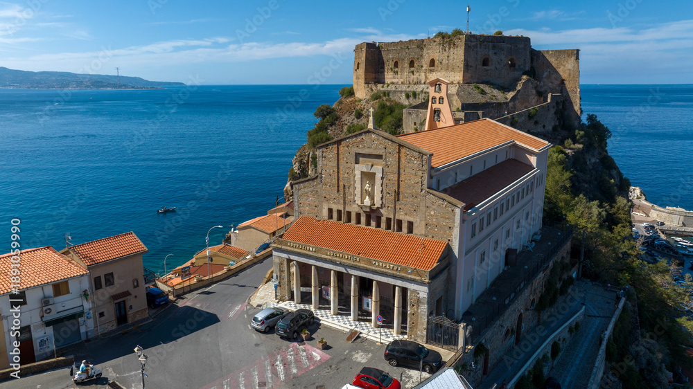 Fototapeta premium Aerial closeup of the main church and the Ruffo Castle located in the historic center of the town of Scilla, Calabria, Italy. It is a village located on a promontory overlooking the Mediterranean sea.