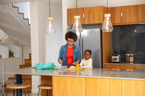 African american mother and daughter packing lunch on kitchen island slicing sandwich