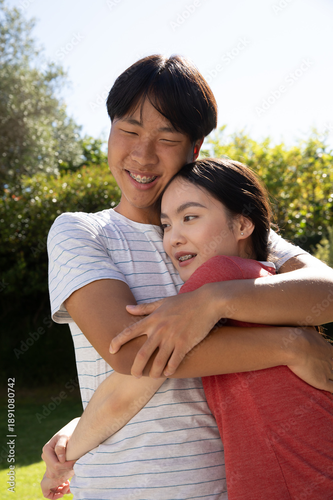 Naklejka premium Asian couple hugging standing on lawn in backyard under sunlight showing braces and earrings