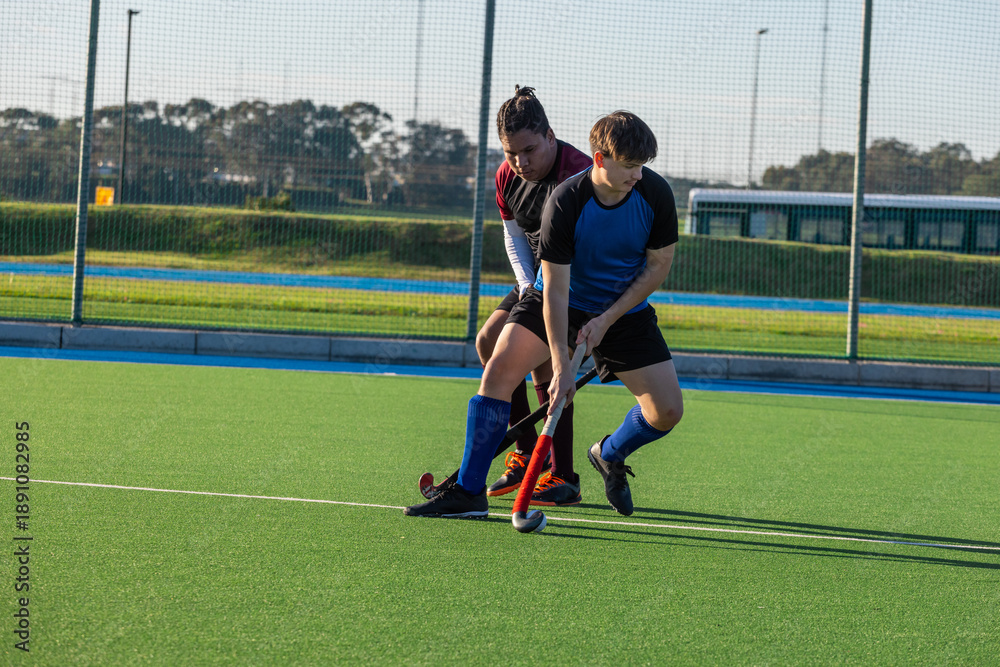 Obraz premium Diverse male field hockey players competing for white ball on turf pitch with sticks