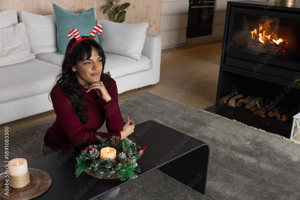 Fototapeta premium Woman leaning on black coffee table by fireplace in living room with wreath, candle