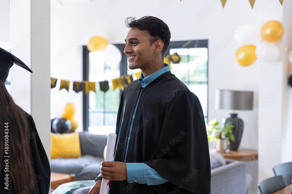 Naklejka premium Asian friends celebrating graduation inside decorated living room with gowns balloons, diploma