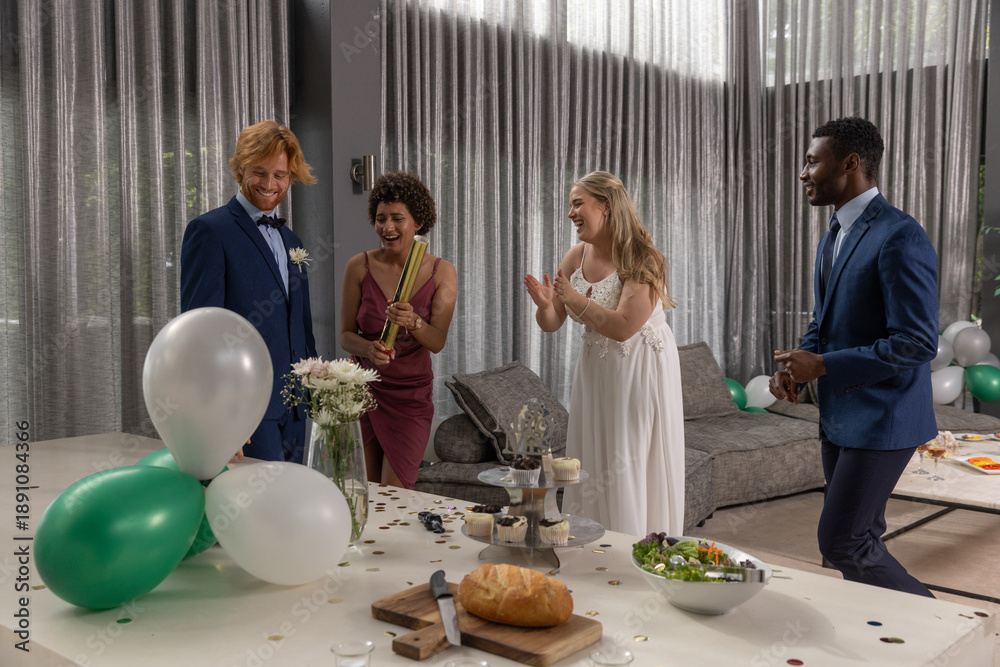Naklejka premium Diverse friends and newlyweds in formal wear celebrating at table in living room