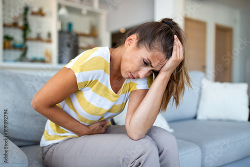 Фотография Woman holding head and stomach in pain sitting on couch