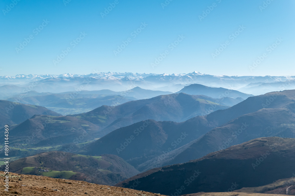Naklejka premium A vastidão das camadas montanhosas de Iparralde sob uma névoa suave, com a cordilheira dos Pirenéus em destaque no horizonte azul em França