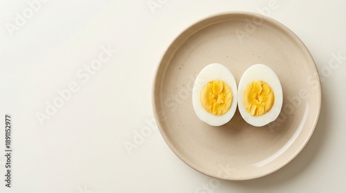 Sliced boiled egg halves on beige plate against soft background -  