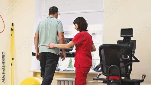 A man recovers from an injury on a treadmill under the guidance of a physical therapist. Stroke rehabilitation, physical activity.