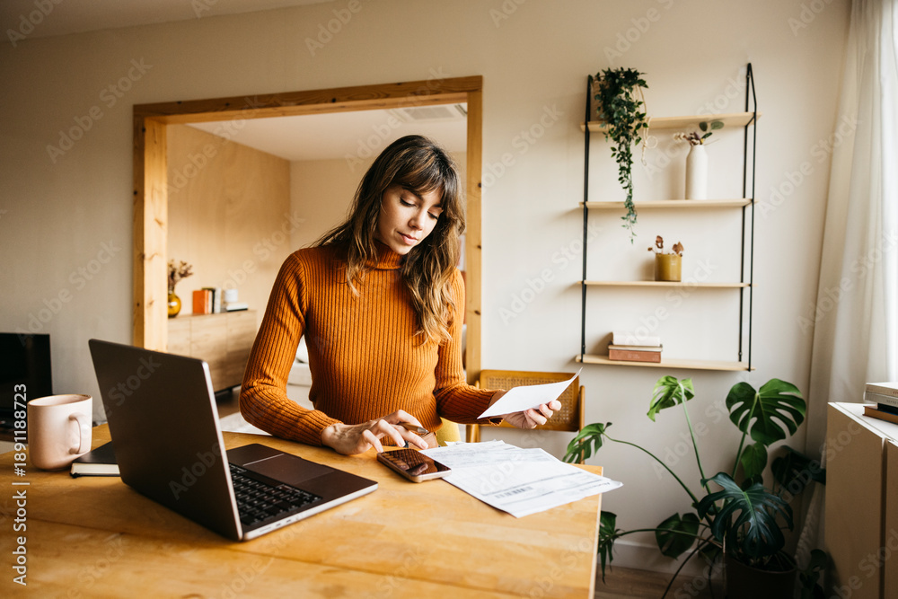 Fototapeta premium Woman managing invoices and finances at home office using laptop