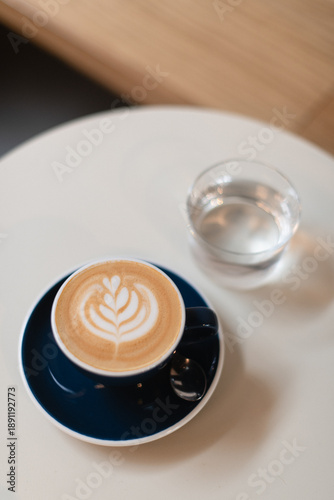 Cappuccino Served in a Blue Cup on a White Round Table with a Glass of Water