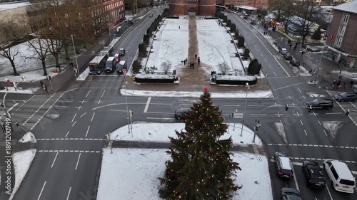 Descending drone shot with tilt up of decorated Christmas tree in Lübeck with Holstentor Gate framed by a snow-covered park in the background.