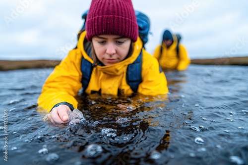 Documentary photograph of two diverse environmental scientists, wearing waders and field gear, collecting water and soil samples in a peatland bog