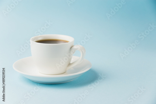 Espresso in a white cup on a blue paper background with copy space. Concept of morning planning for the day