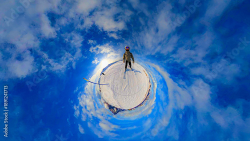 A creative 360-degree projection of a skier standing on the snow-capped peaks of the Seiser Alm in the Dolomites. The spherical panorama is captivating, with a bright blue sky and light clouds.