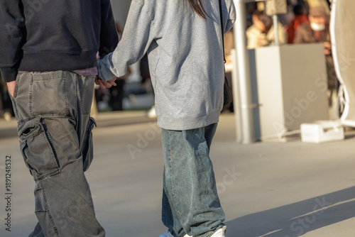 Cuadro en lienzo Young couple wearing oversized streetwear walk hand in hand through outdoor plaza sunlit by warm golden hour sun